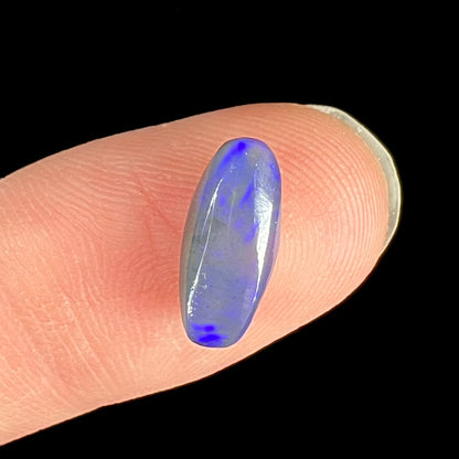 A loose, oval cabochon cut black opal stone that weighs 1.52 carats.  The opal plays blue colors.