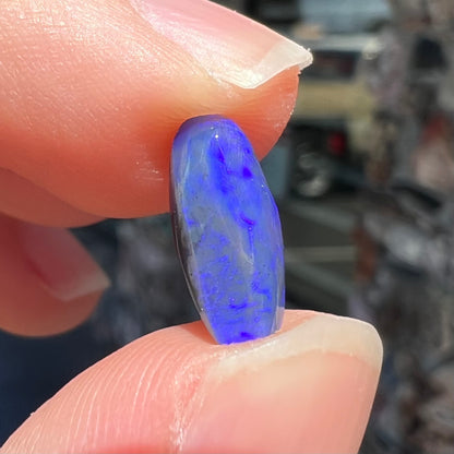 A loose, oval cabochon cut black opal stone that weighs 1.52 carats.  The opal plays blue colors.