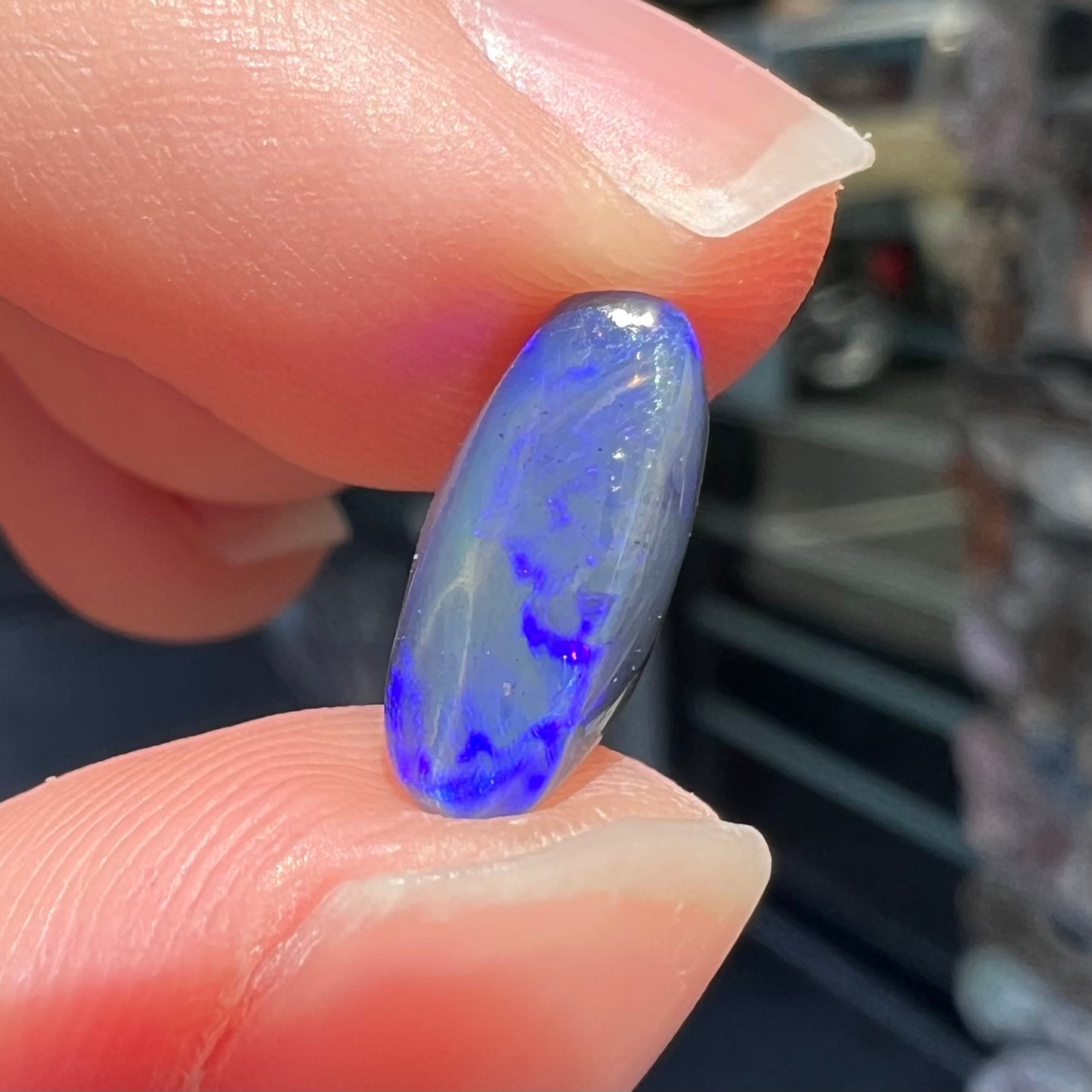 A loose, oval cabochon cut black opal stone that weighs 1.52 carats.  The opal plays blue colors.