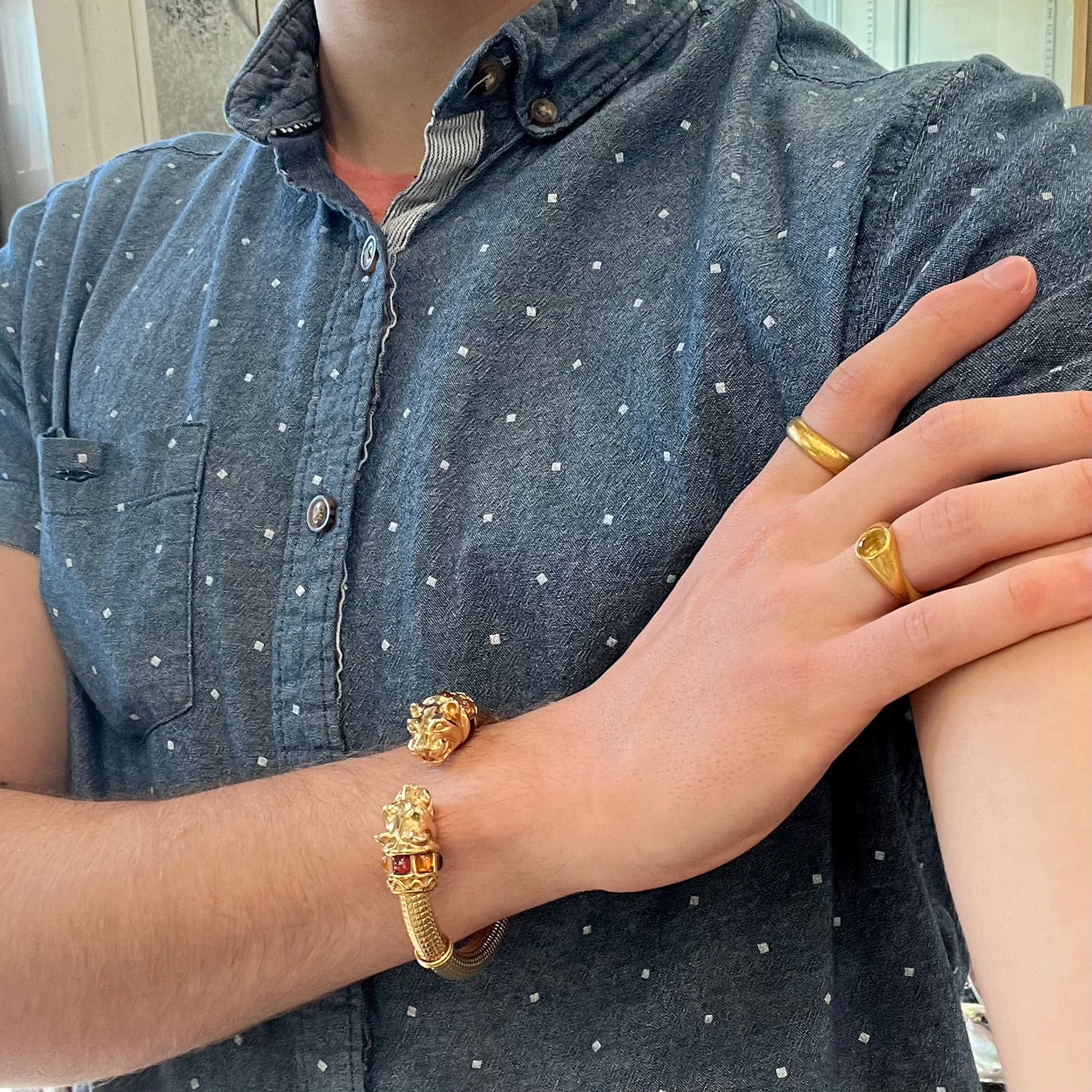 A 14 karat yellow gold hinged bangle bracelet featuring the motif of two panther heads.  There are yellow and red accent stones.