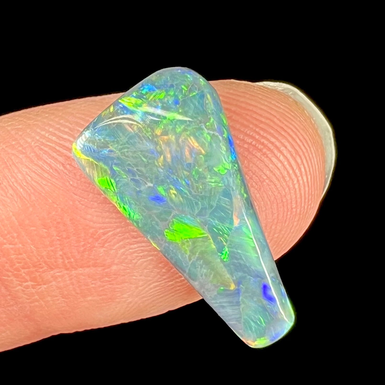 A loose, freeform triangle shaped black opal stone from Lightning Ridge, Australia that weighs 2.71 carats.