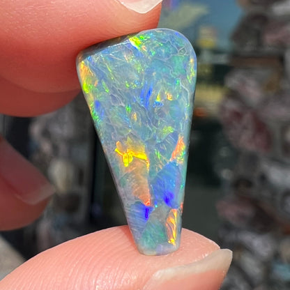 A loose, freeform triangle shaped black opal stone from Lightning Ridge, Australia that weighs 2.71 carats.