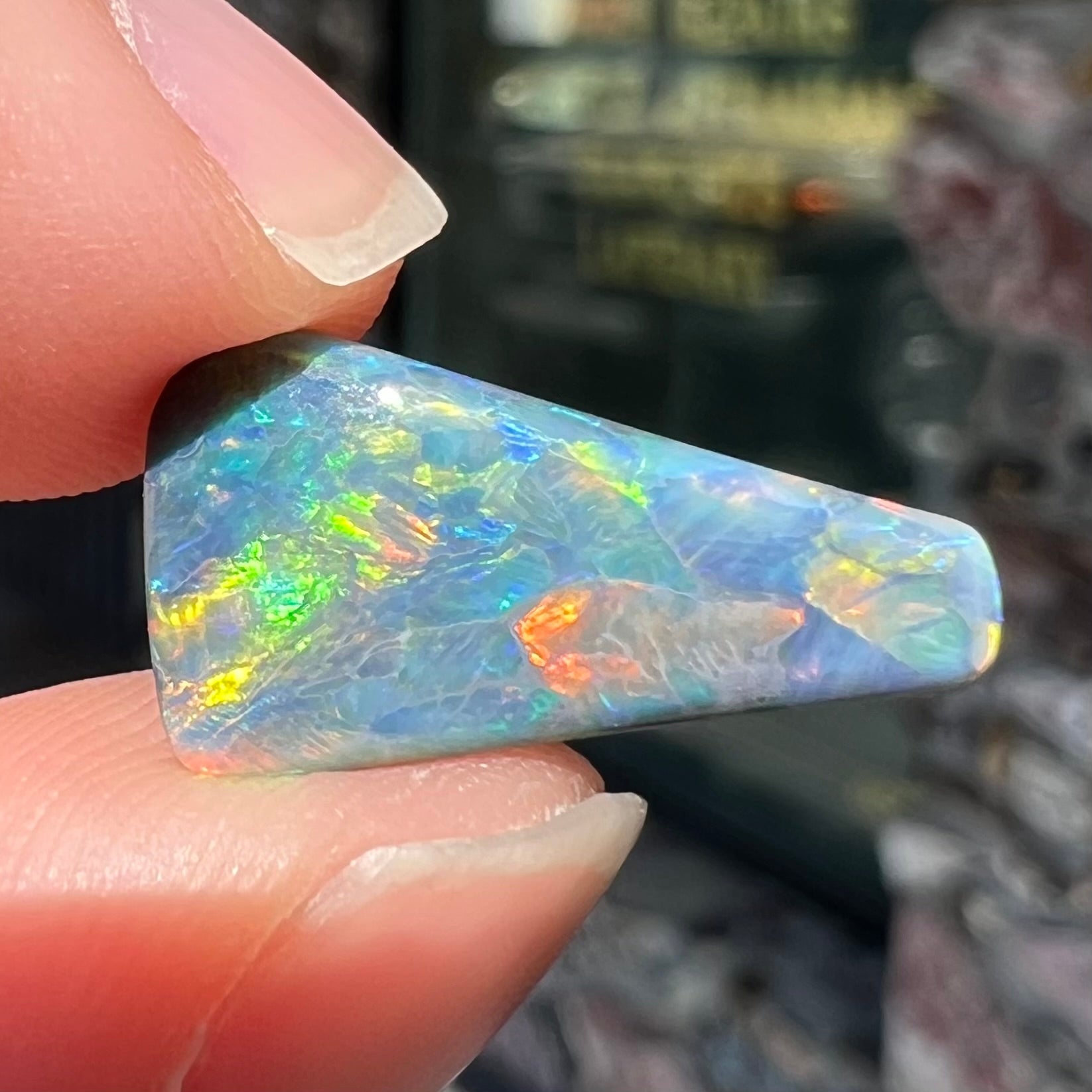 A loose, freeform triangle shaped black opal stone from Lightning Ridge, Australia that weighs 2.71 carats.