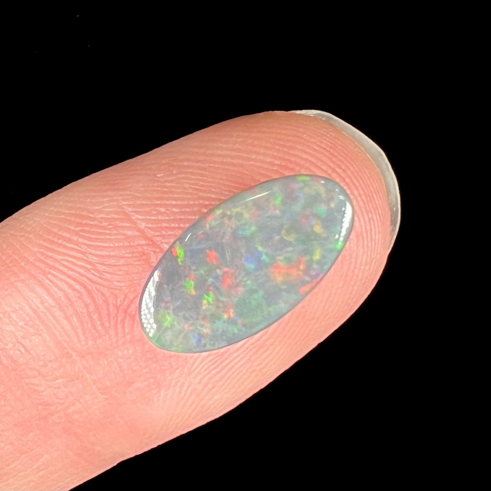 A loose, 3.01 carat, oval cut semi-black opal stone from Lightning Ridge, Australia.  The opal has red colors.