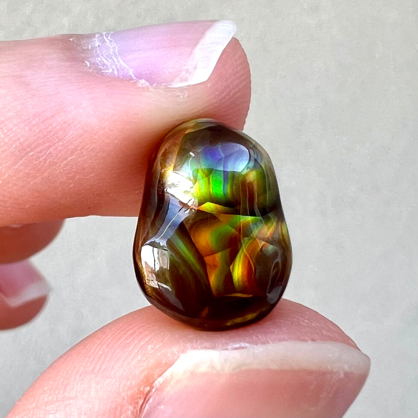 A loose, freefrom cabochon cut Mexican fire agate stone.  The stone has red, green, yellow, and purple banding.