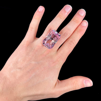 A loose, radiant cut kunzite gemstone.  The stone is a light purplish pink color.