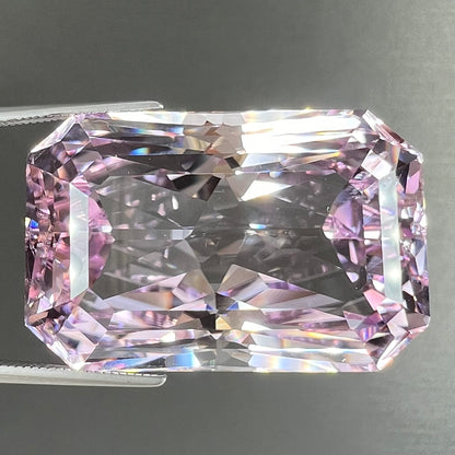 A loose, radiant cut kunzite gemstone.  The stone is a light purplish pink color.