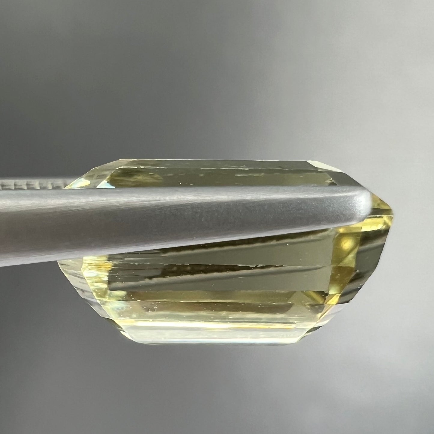 A loose, emerald cut hiddenite gemstone.  The stone is a light yellow green color.