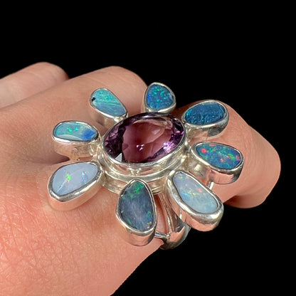 A sterling silver flower shaped ring set with an oval cut amethyst in the center and black opal doublet petals.