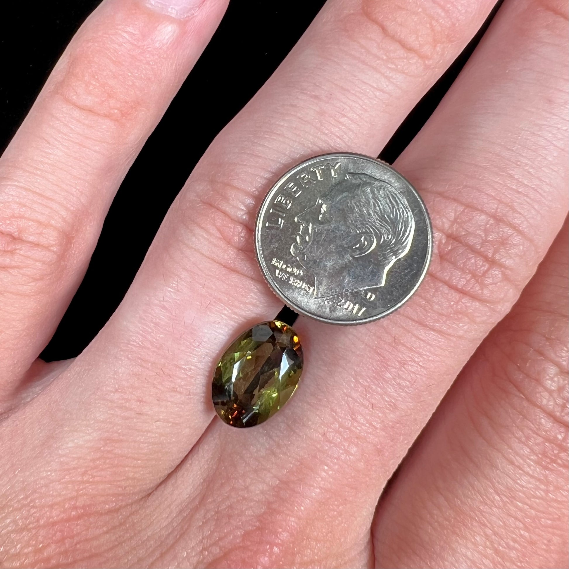 A loose, faceted oval cut andalusite gemstone.  The stone shows brown and green colors.