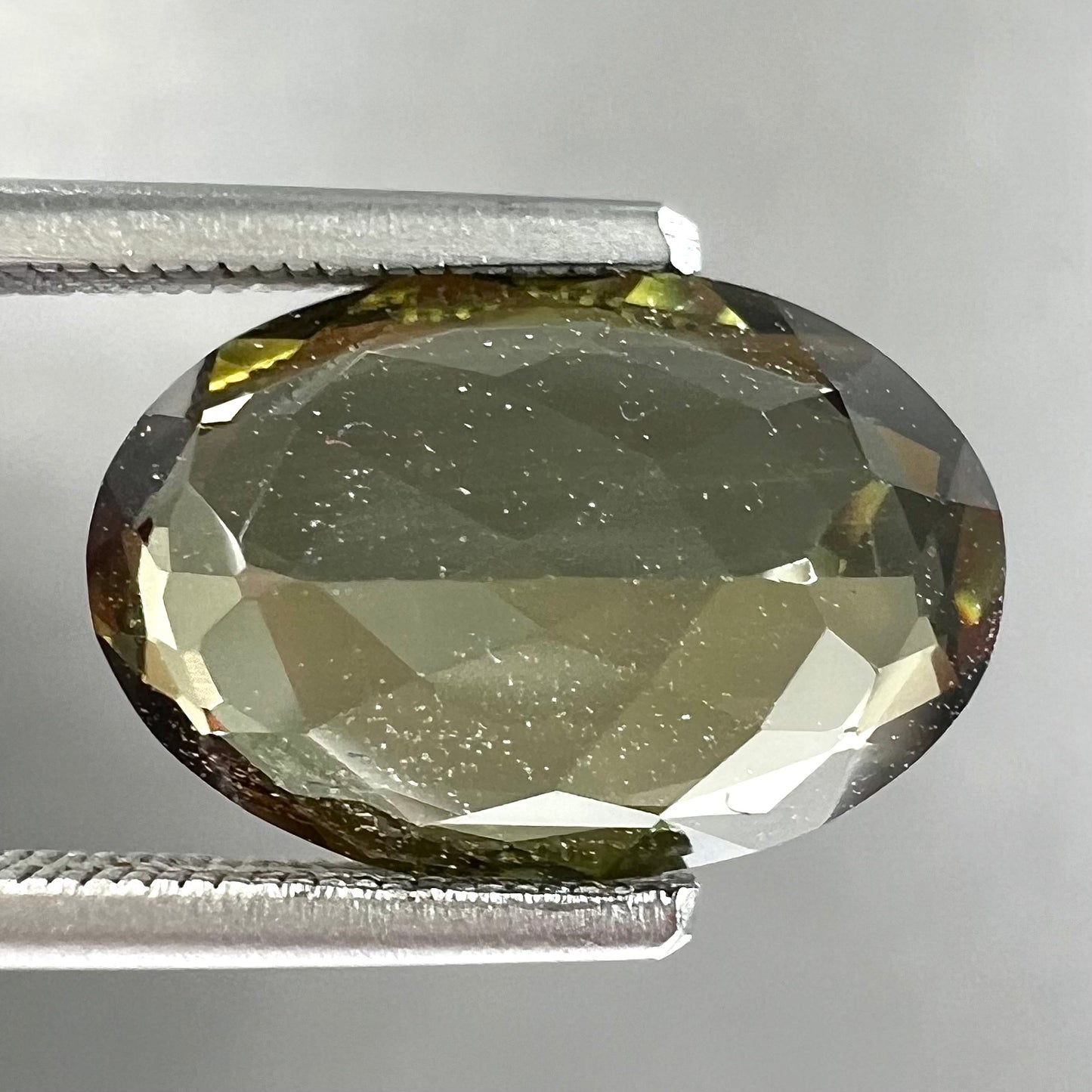 A loose, faceted oval cut andalusite gemstone.  The stone shows brown and green colors.