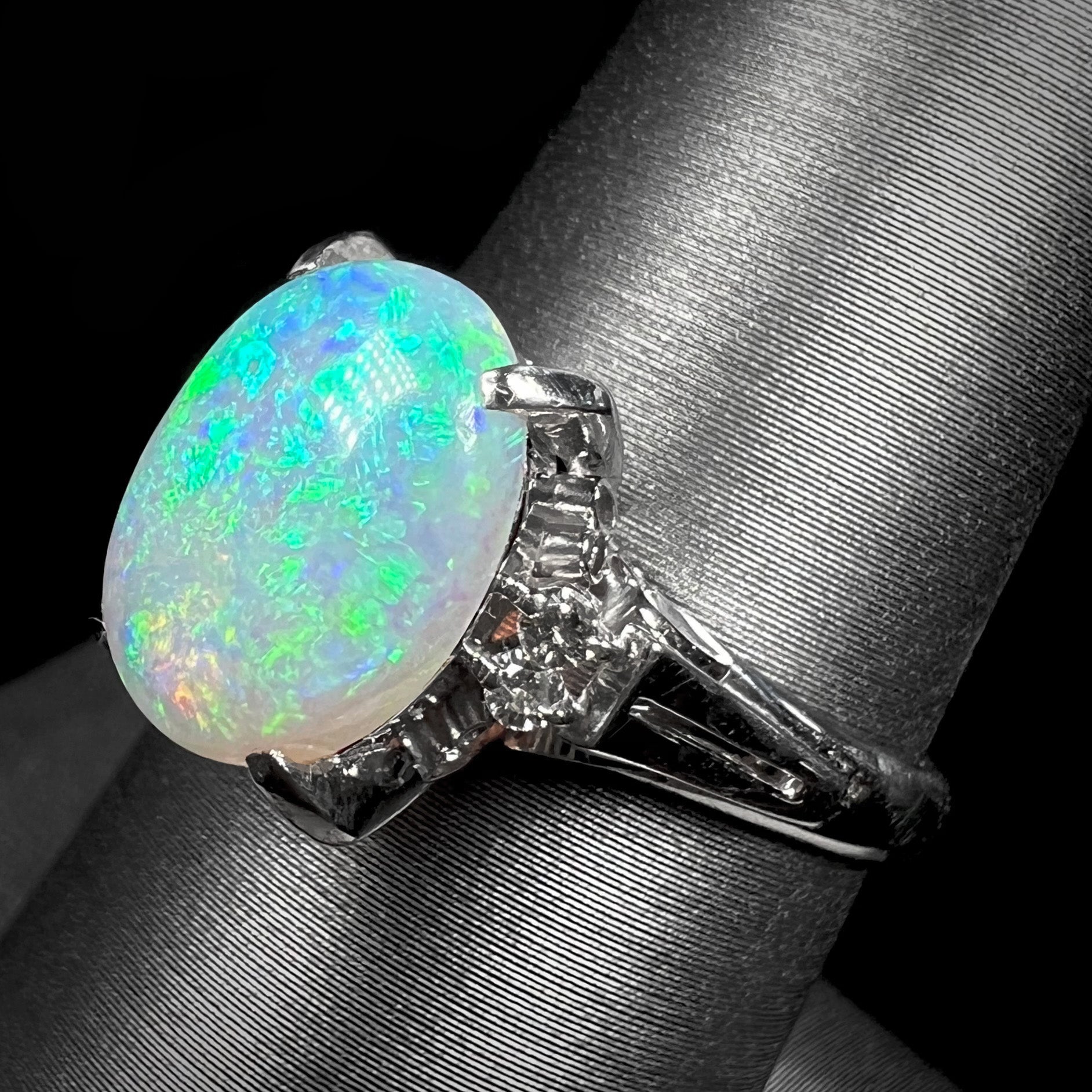 A platinum filigree opal engagement ring set with diamond accents.  The opal has green-blue colors.