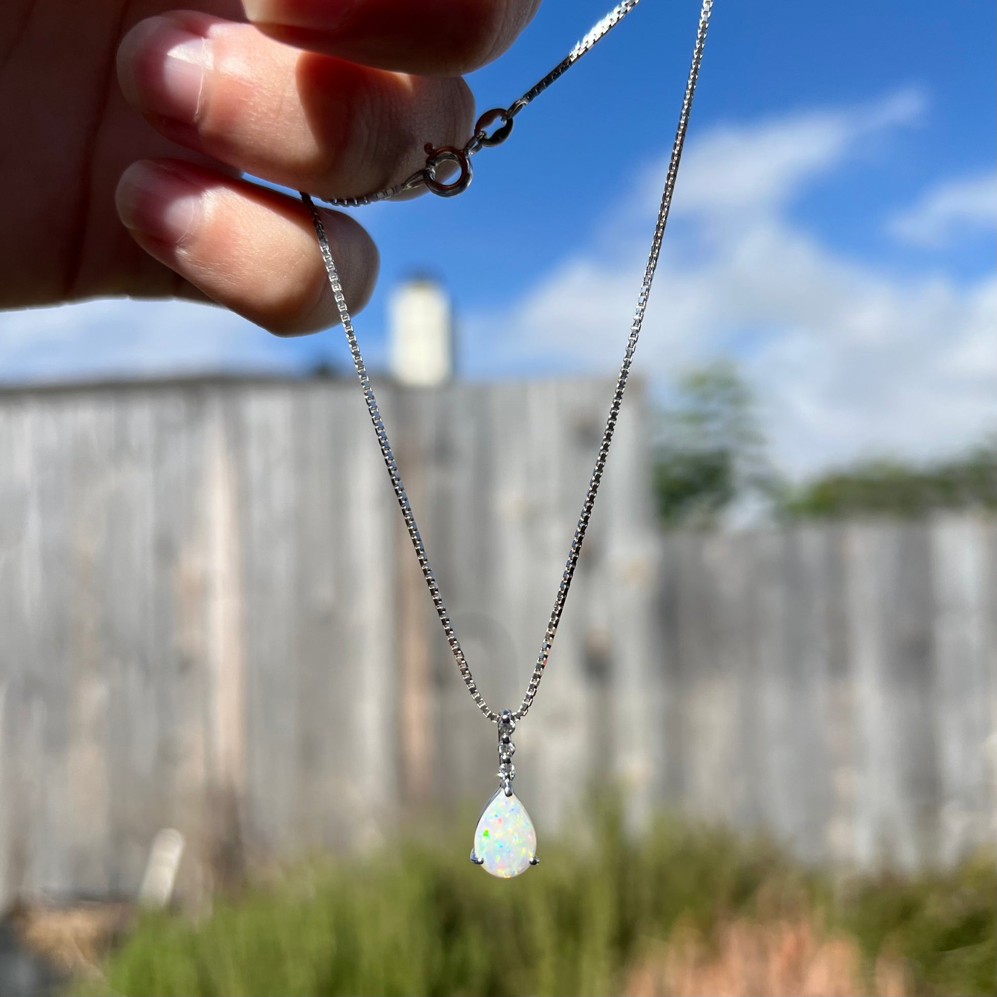 A platinum drop pendant mounted with three diamond accents and a pear shaped opal.