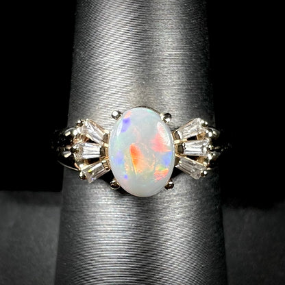 A yellow gold ring set with a natural Australian opal and tapered baguette cut cubic zirconia accents.