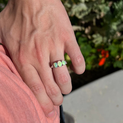 A ladies' white gold ring prong-set with three natural white opals and diamond accents.  The opals play a green color.