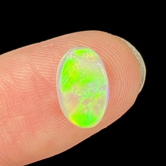 An oval cabochon cut white opal stone from Coober Pedy, Australia.  The opal brilliantly shines green and orange colors.