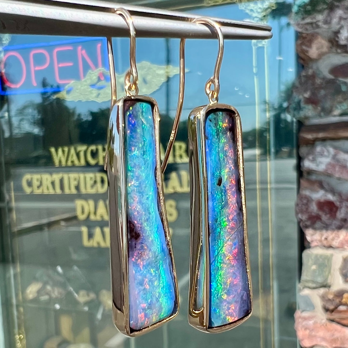 A pair of natural boulder opal dangle earrings set in yellow gold.  The opal displays a rainbow of colors and is from Bull Creek, Australia.