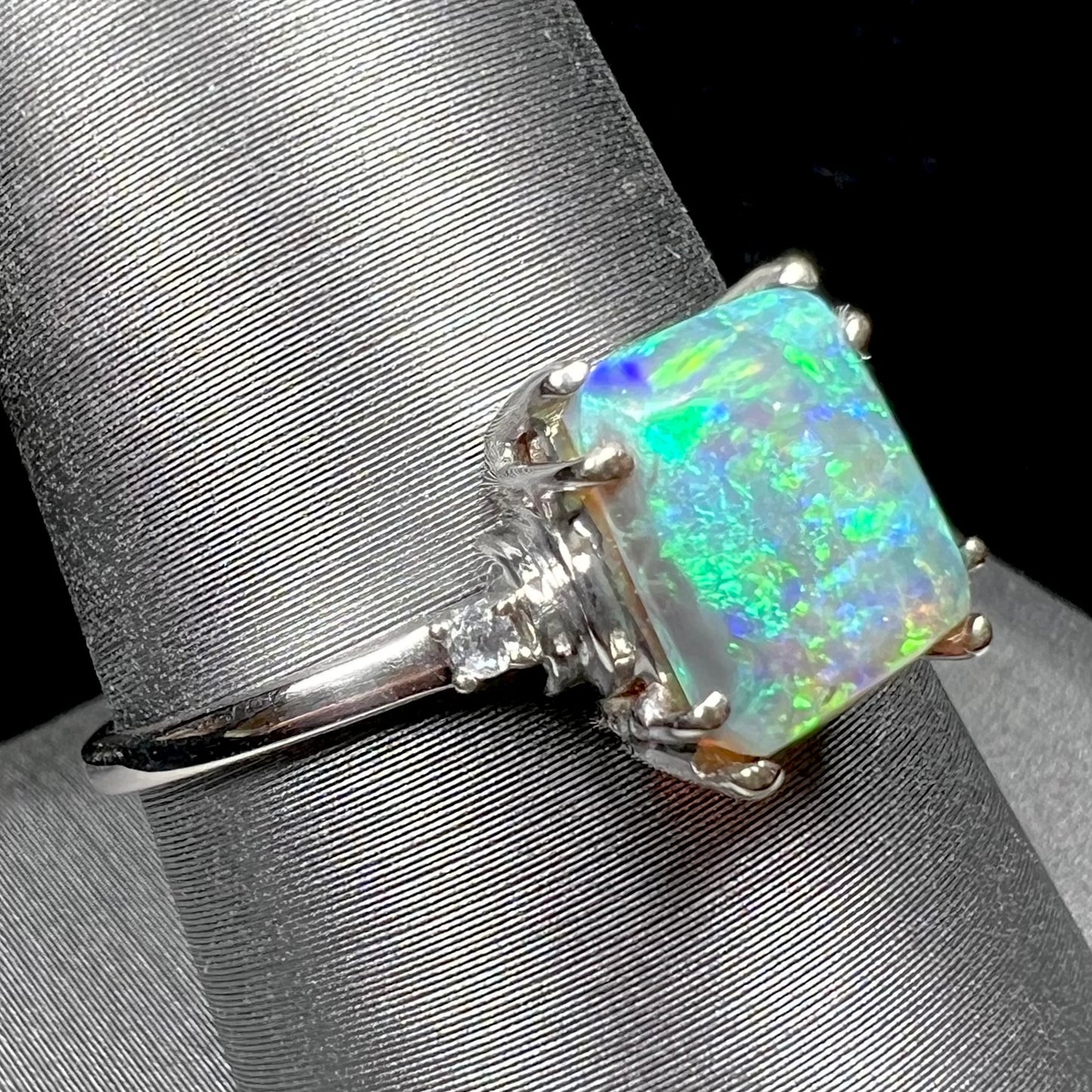 A ladies' white gold ring set with a rectangle cut black opal stone with round white sapphire accent stones.