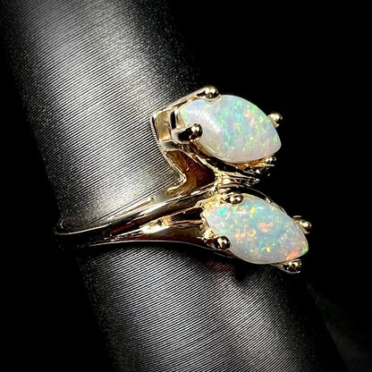 A yellow gold ring mounted with two prong-set marquise cut opal cabochons.