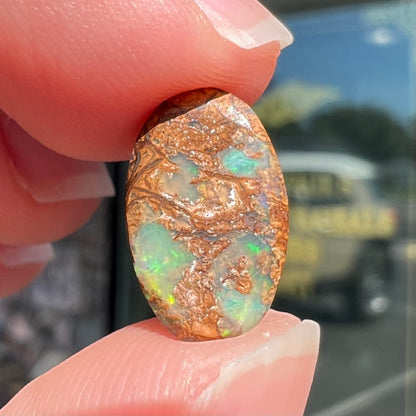 A loose, oval cabochon cut Koroit boulder opal with green fire.