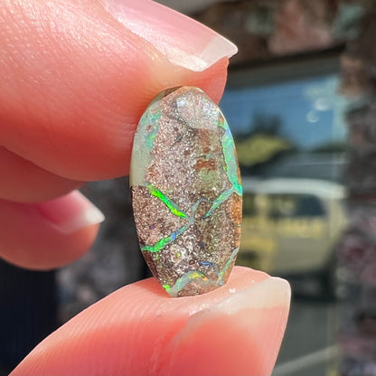 A loose, oval cabochon cut Koroit boulder opal stone.  The opal has a bright green color.