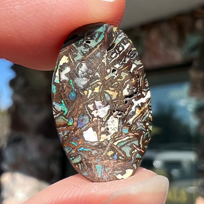 A loose, oval cabochon cut Koroit boulder opal stone.  The opal has green and blue veins.