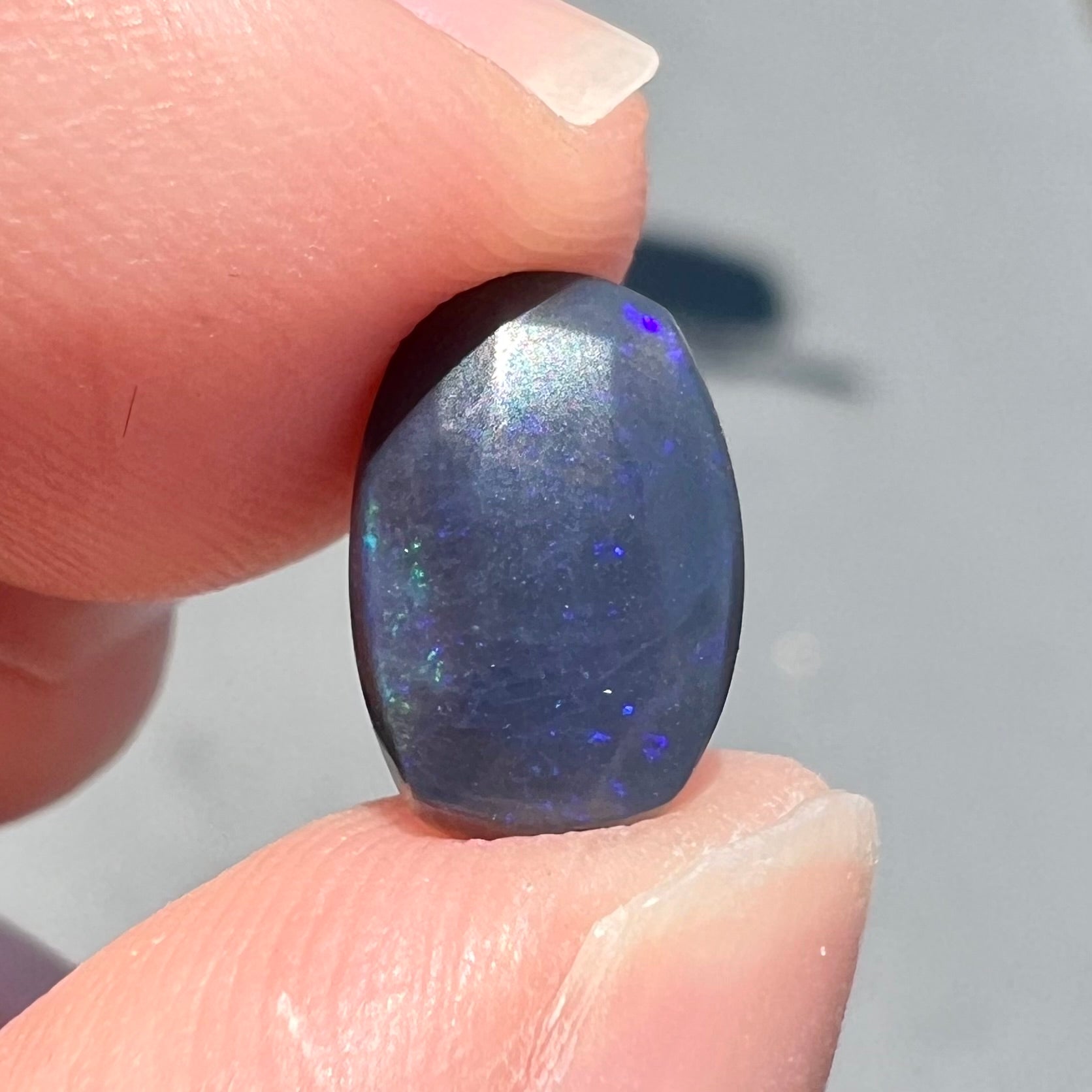 A loose Lightning Ridge black opal stone that shines colors of green, blue, and purple.