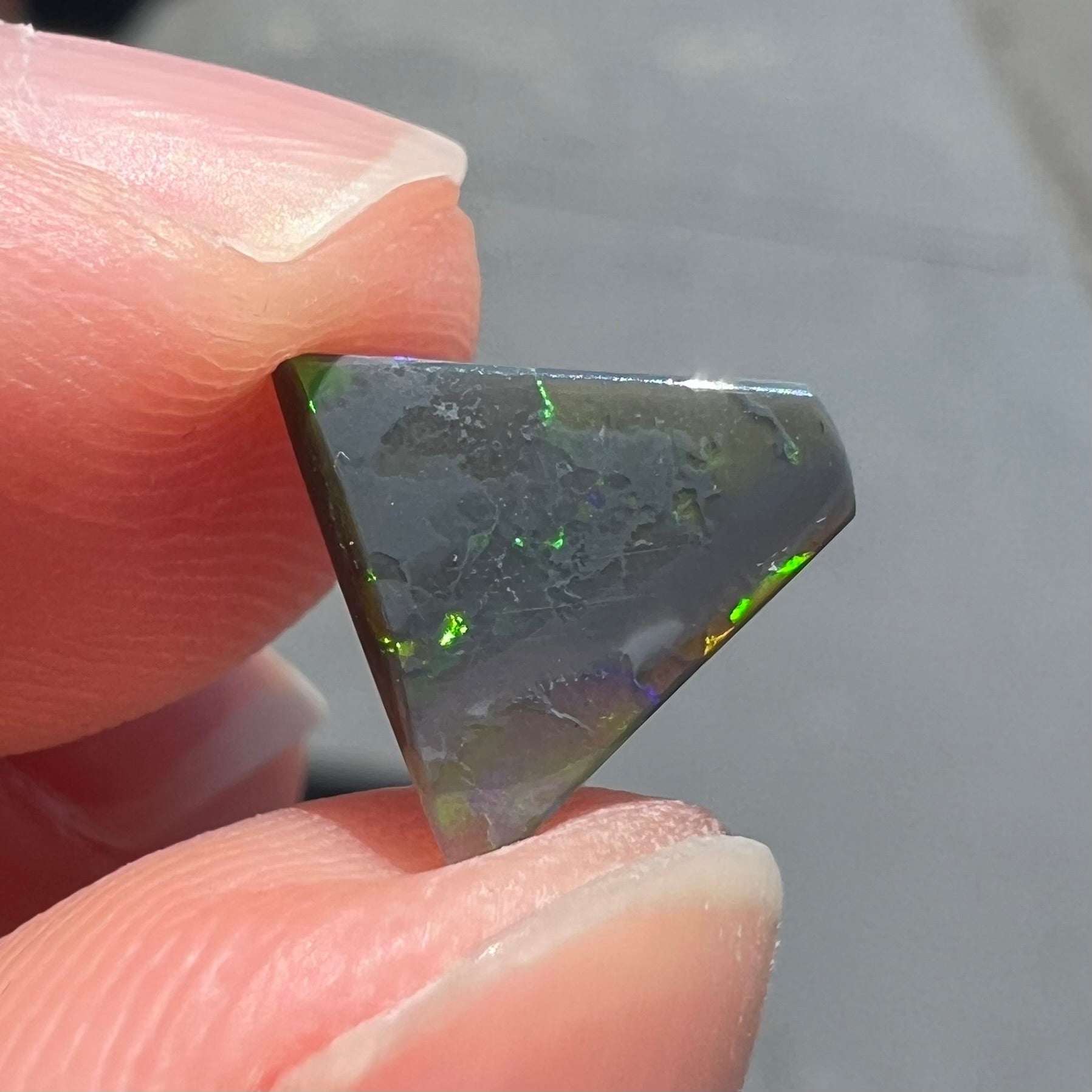 A loose, triangular shaped black opal from Lightning Ride, Australia.  The opal is predominantly green.