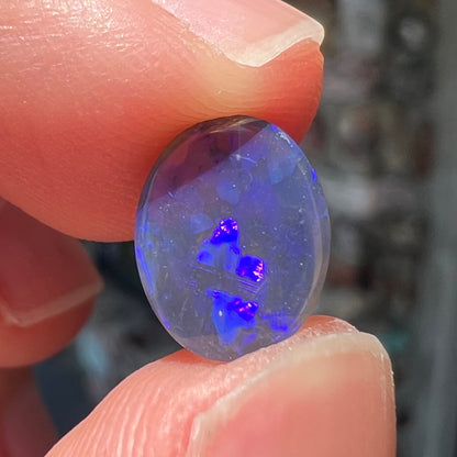 A loose, oval cabochon cut black crystal opal from Lightning Ridge, Australia.