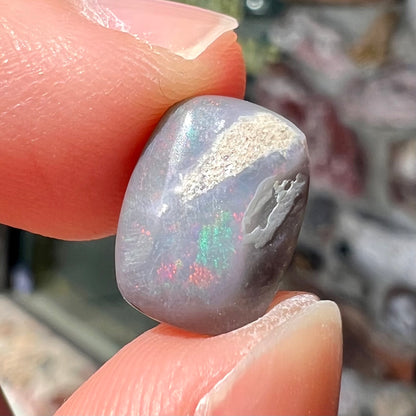 A loose, cushion cut black opal stone.  The stone plays colors of red, green, blue, and purple.