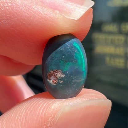 A loose, oval cabochon cut black opal from Lightning Ridge, Australia.  The opal has an N2 body tone.