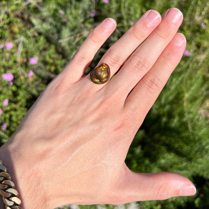 A large, round freeform shaped Mexican fire agate stone.  The stone has green, orange, purple, and blue iridescence.