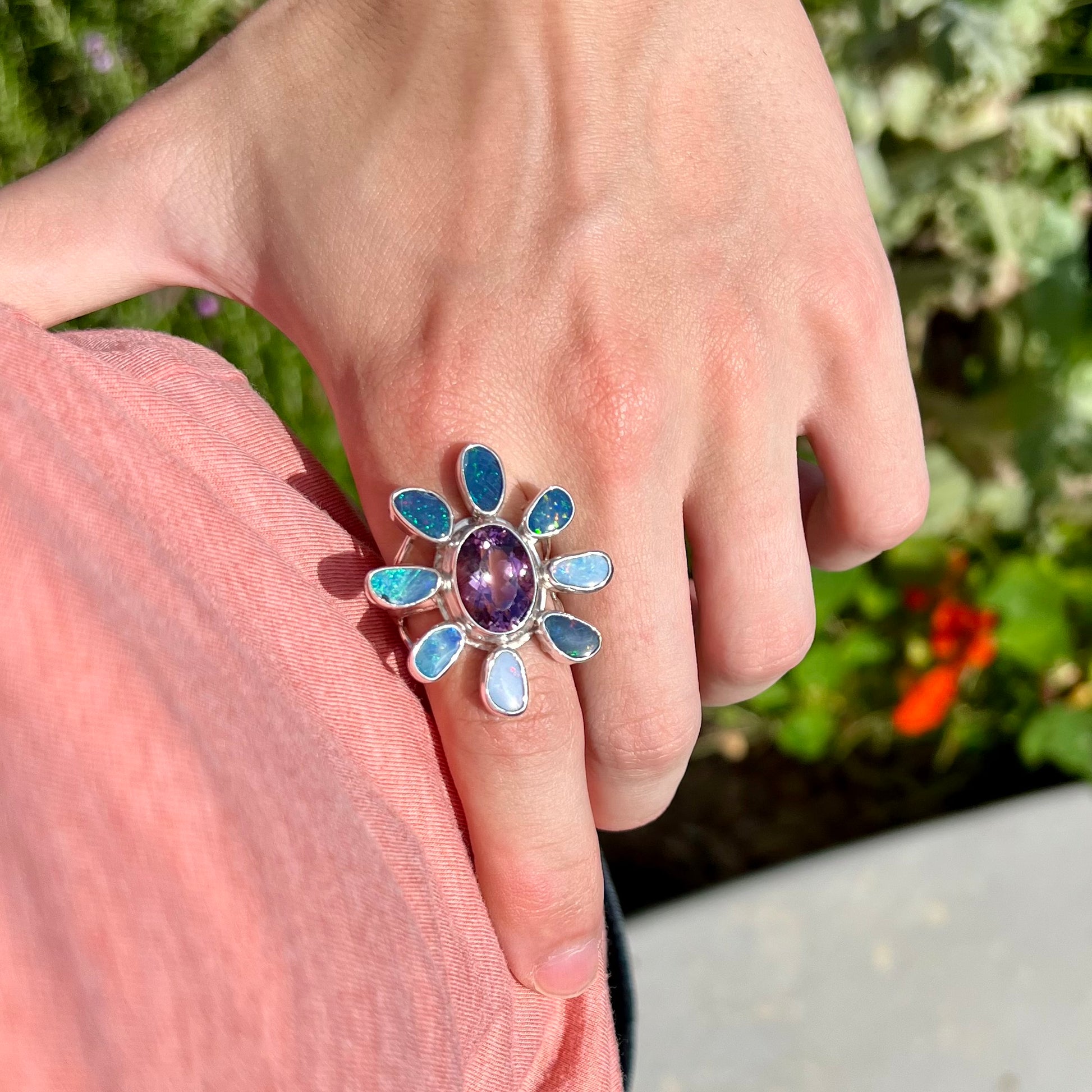 A sterling silver flower shaped ring set with an oval cut amethyst in the center and black opal doublet petals.