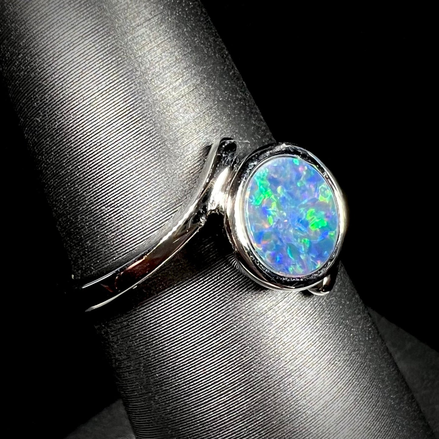 A sterling silver bypass ring bezel-set with a round cut black opal doublet.