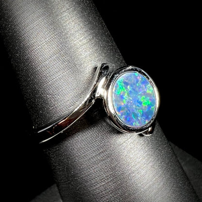 A sterling silver bypass ring bezel-set with a round cut black opal doublet.