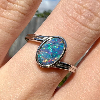 A sterling silver ring bezel-set with an oval shaped black opal doublet.  The opal has red and blue fire.