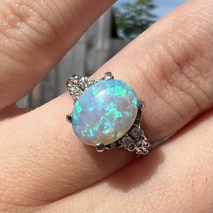 A black crystal opal platinum ring with diamond accents and filigree.