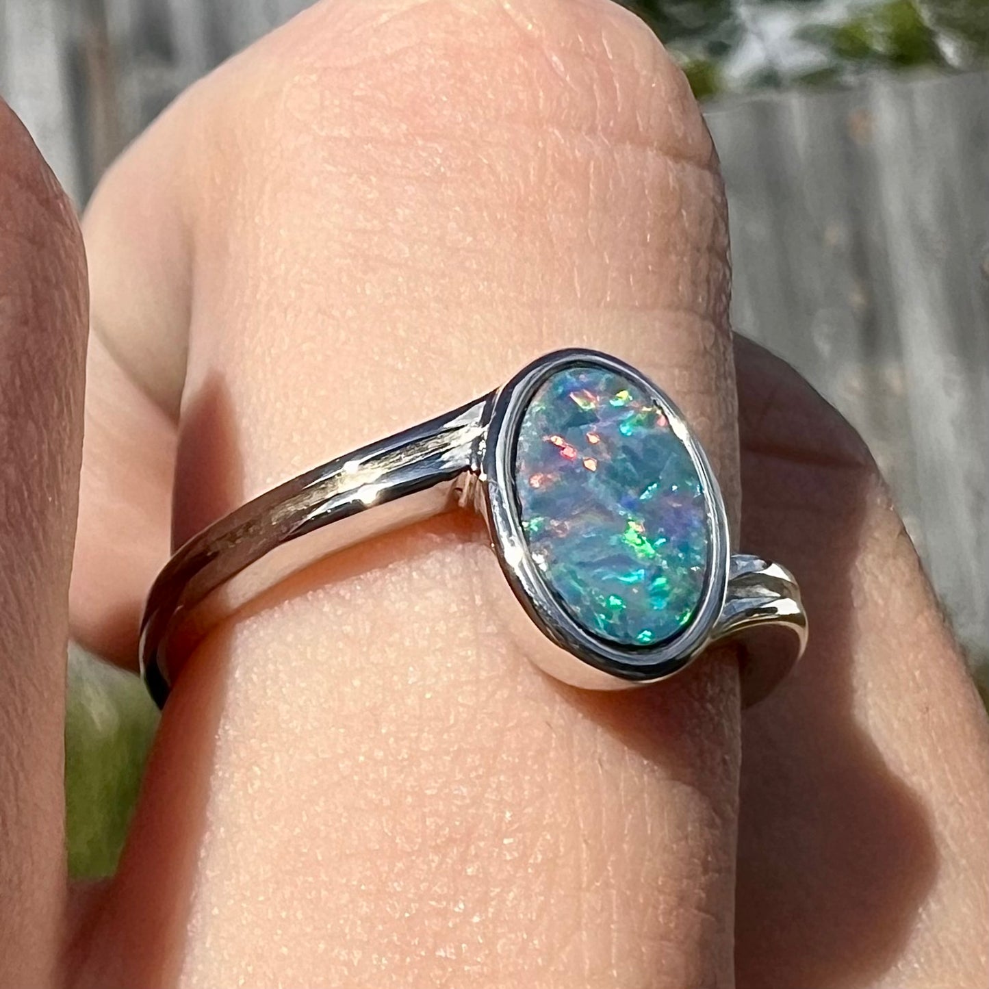 A sterling silver ring bezel-set with an oval shaped black opal doublet.  The opal has red and blue fire.