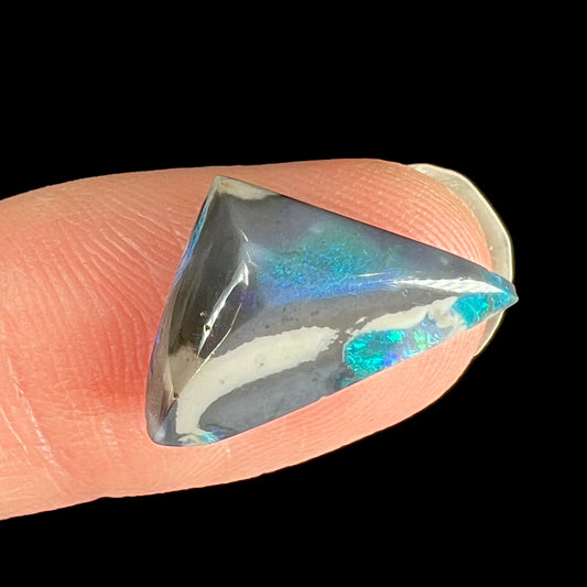 A loose, triangle shaped black opal stone from Lightning Ridge, Australia.  The opal has different colors of black and semi-black opal potch.