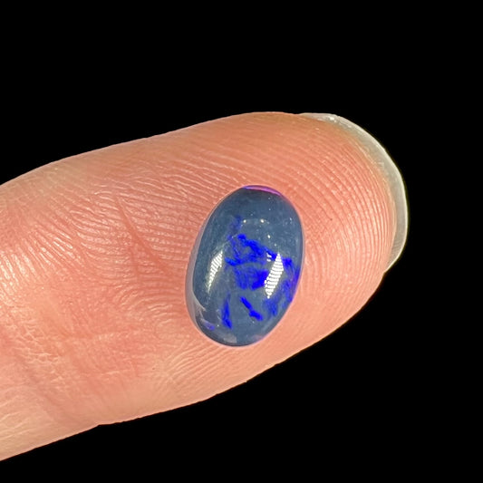 A loose, oval cabochon cut black opal stone from Lightning Ridge, Australia.  The opal has an N2 body tone.