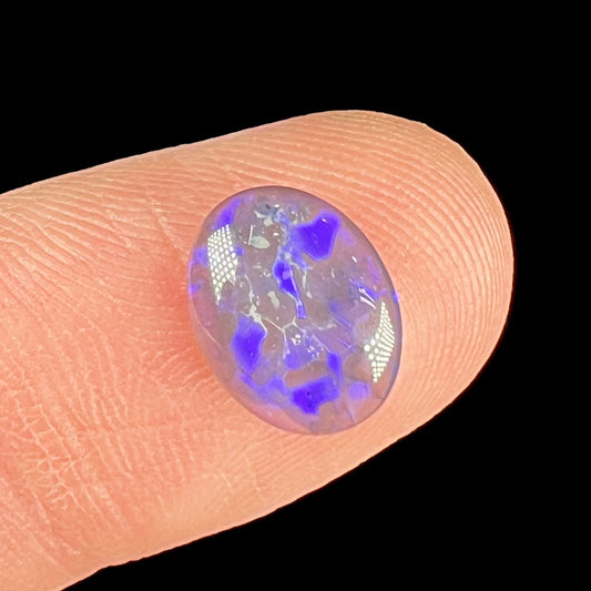 A loose, oval cabochon cut black crystal opal from Lightning Ridge, Australia.