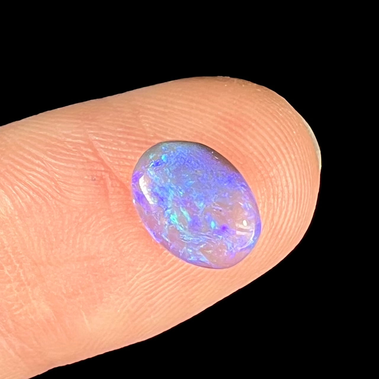 An oval cabochon cut black crystal opal.  The opal has blue and purple colors.