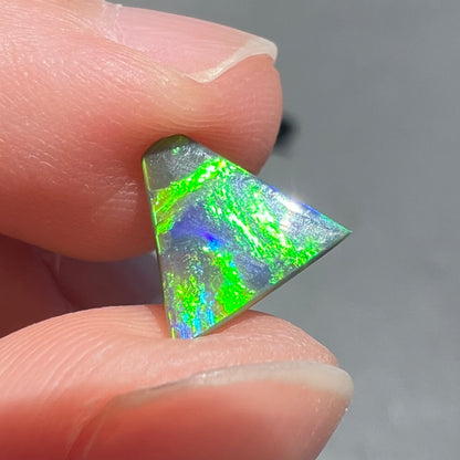 A loose, triangular shaped black opal from Lightning Ride, Australia.  The opal is predominantly green.