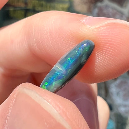 A loose, elongated oval cut black opal that has a green and blue cat's eye.