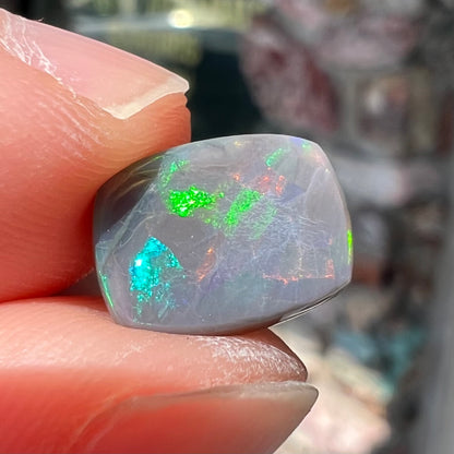 A loose, cushion cut black opal stone.  The stone plays colors of red, green, blue, and purple.