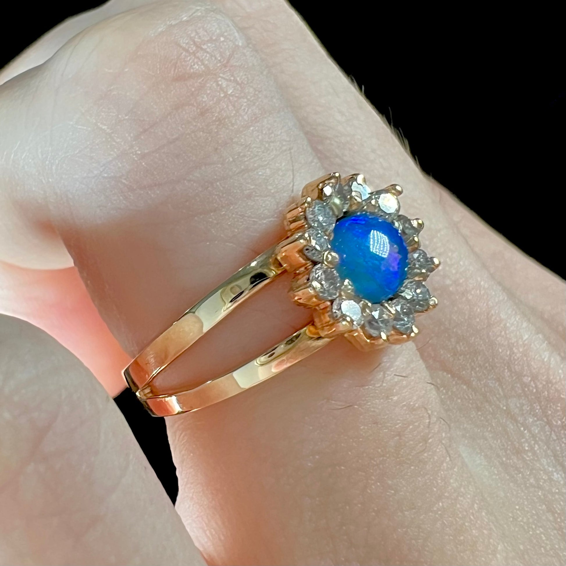 A ladies' round cut black opal and diamond halo ring.  The ring is yellow gold and has a split shank.
