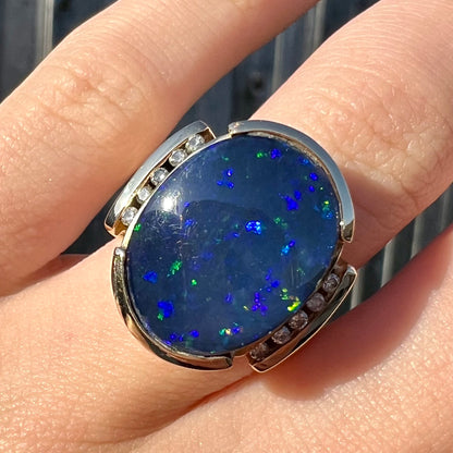 A large, unisex gold ring mounted with a half-bezel set black opal doublet and diamonds.