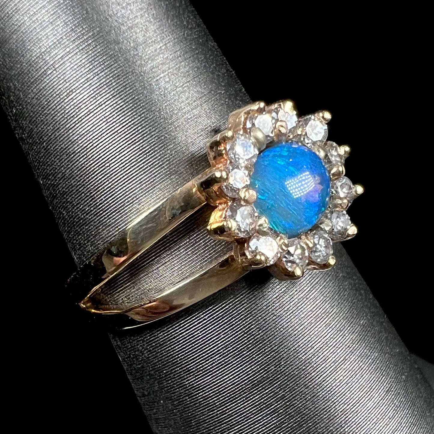 A ladies' round cut black opal and diamond halo ring.  The ring is yellow gold and has a split shank.