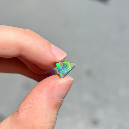 A loose, triangular shaped black opal from Lightning Ride, Australia.  The opal is predominantly green.