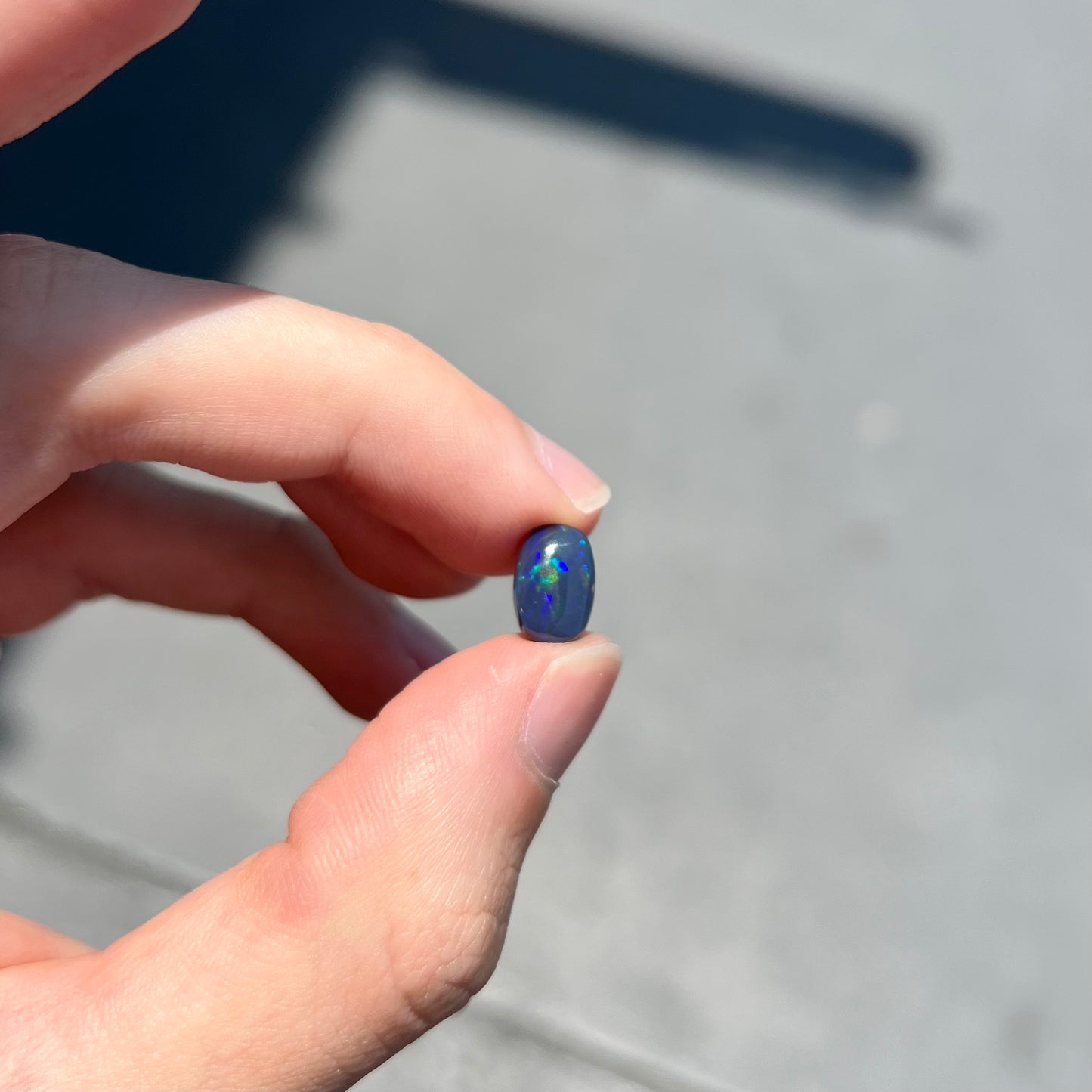 A loose Lightning Ridge black opal stone that shines colors of green, blue, and purple.